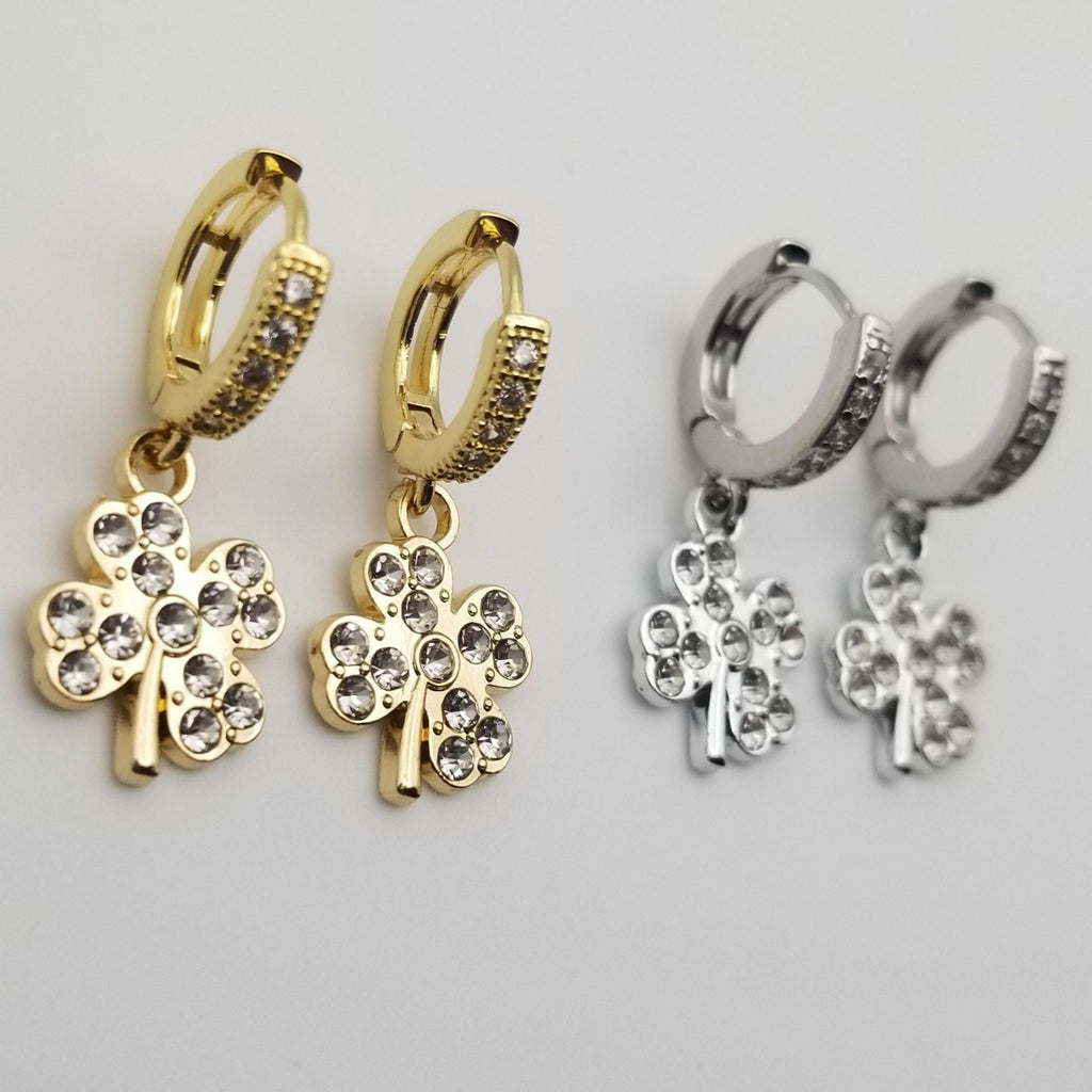 Gold and silver clover-shaped earrings on a light gray background