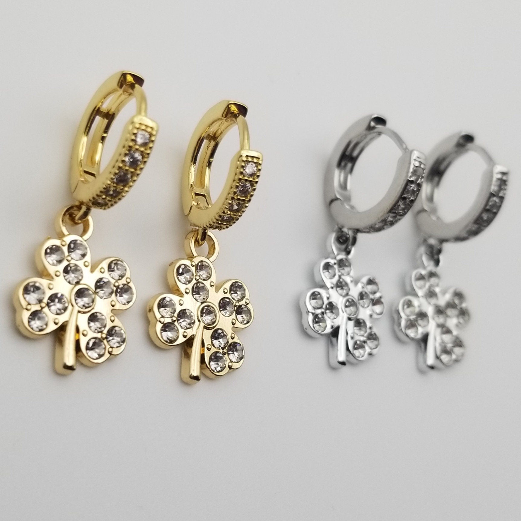 Gold and silver clover-shaped earrings on a light gray background