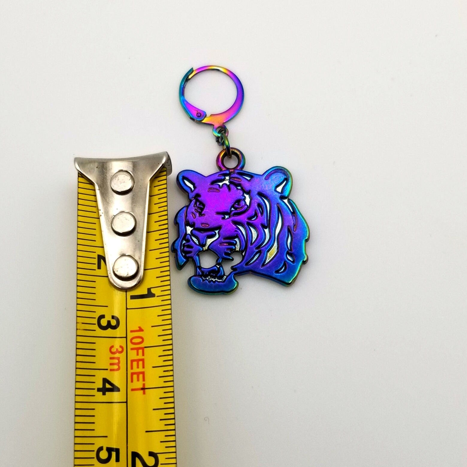 Holographic tiger earring next to a tape measure on a white background