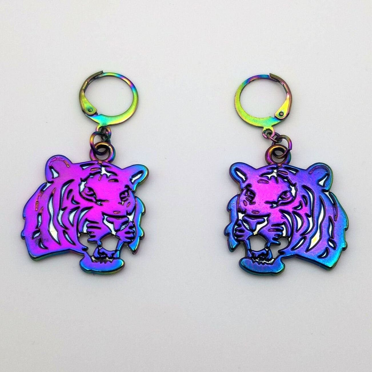 tiger-shaped earrings with a colorful, iridescent finish on a light gray background.