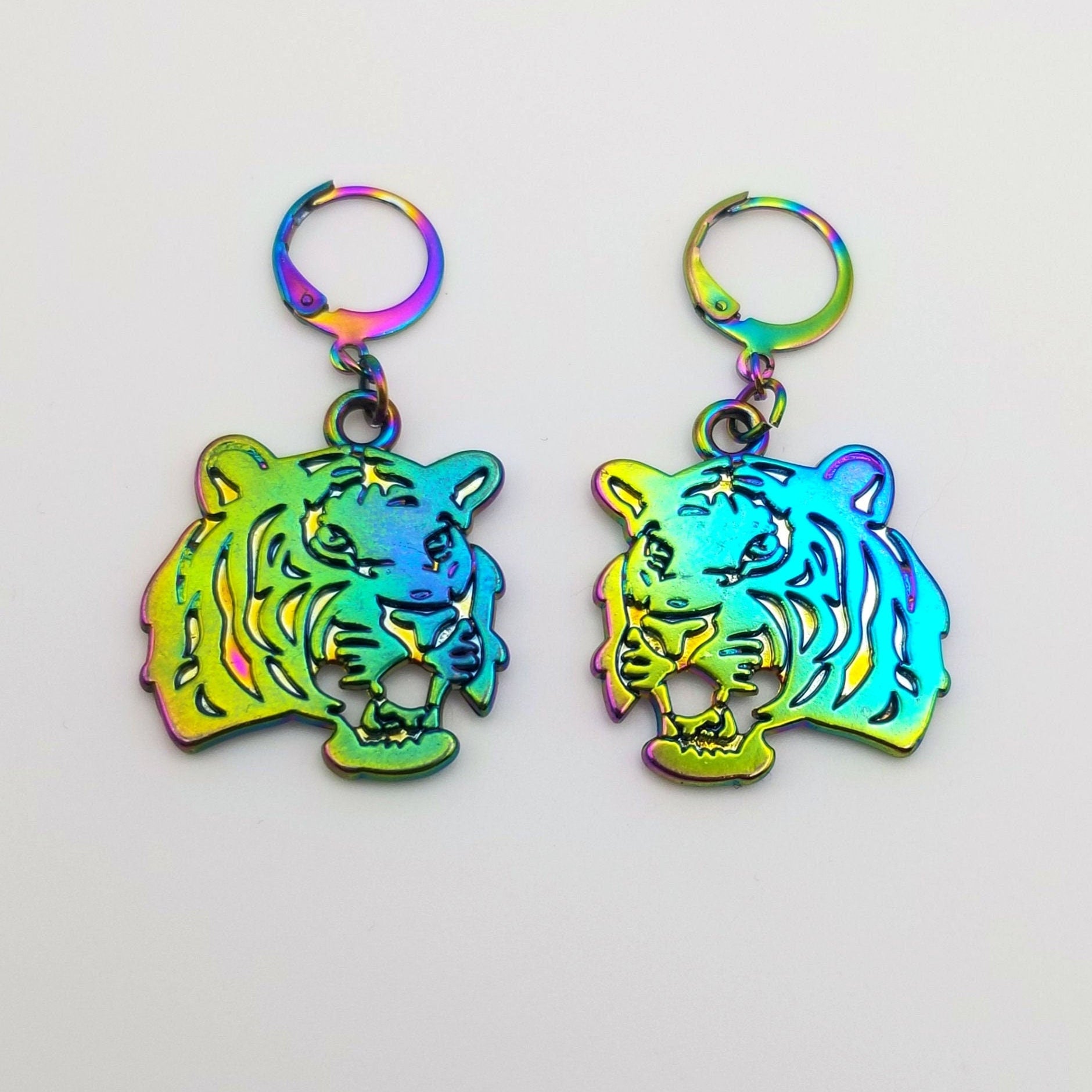 Tiger-shaped Huggie earrings with a rainbow iridescent finish on a light gray background.