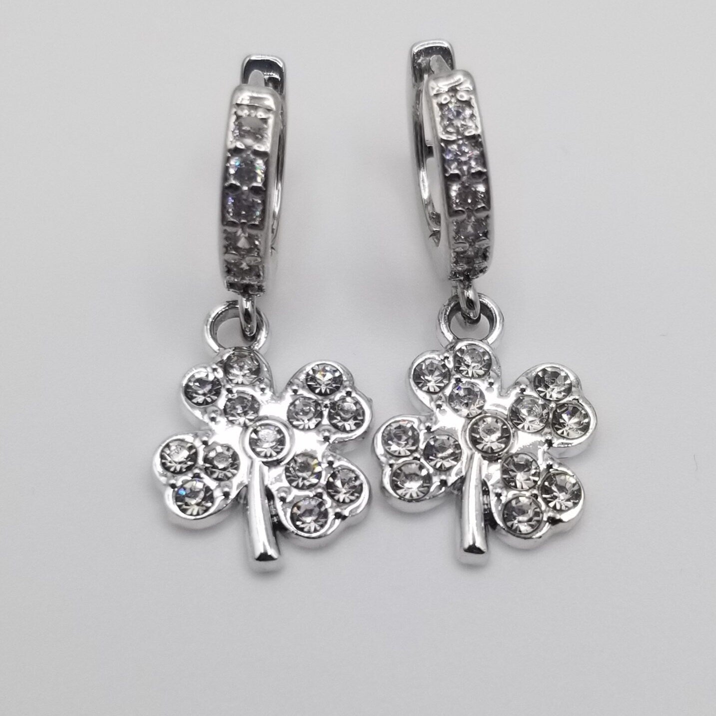 Pair of silver earrings with clover-shaped charms on a gray background