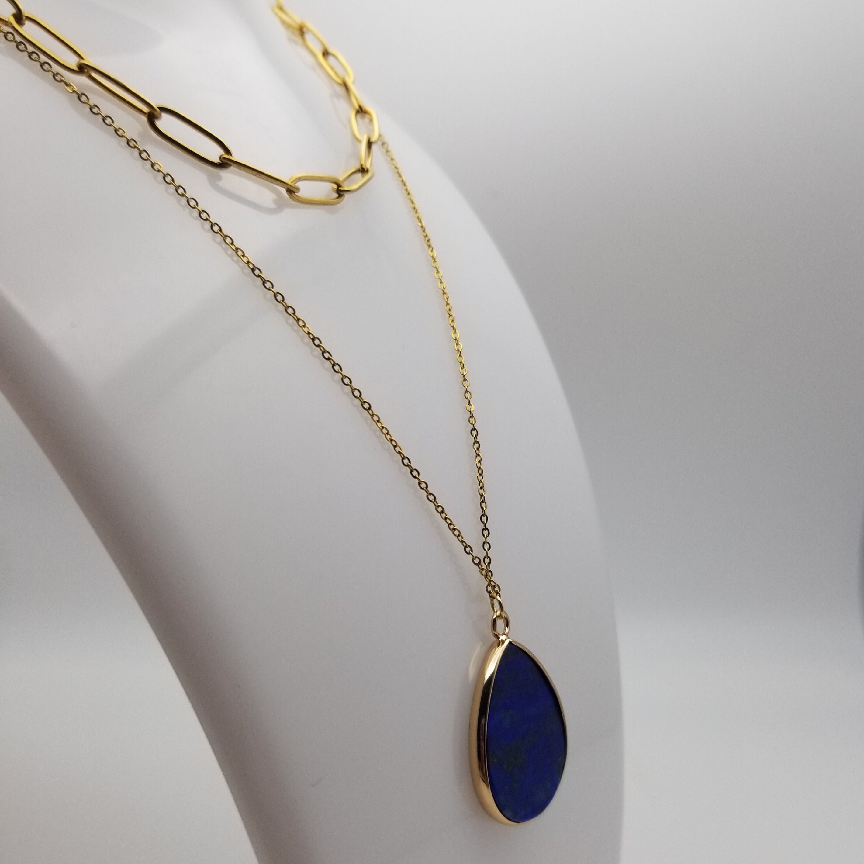 Gold necklace with a blue lapis lazuli pendant on a white stand