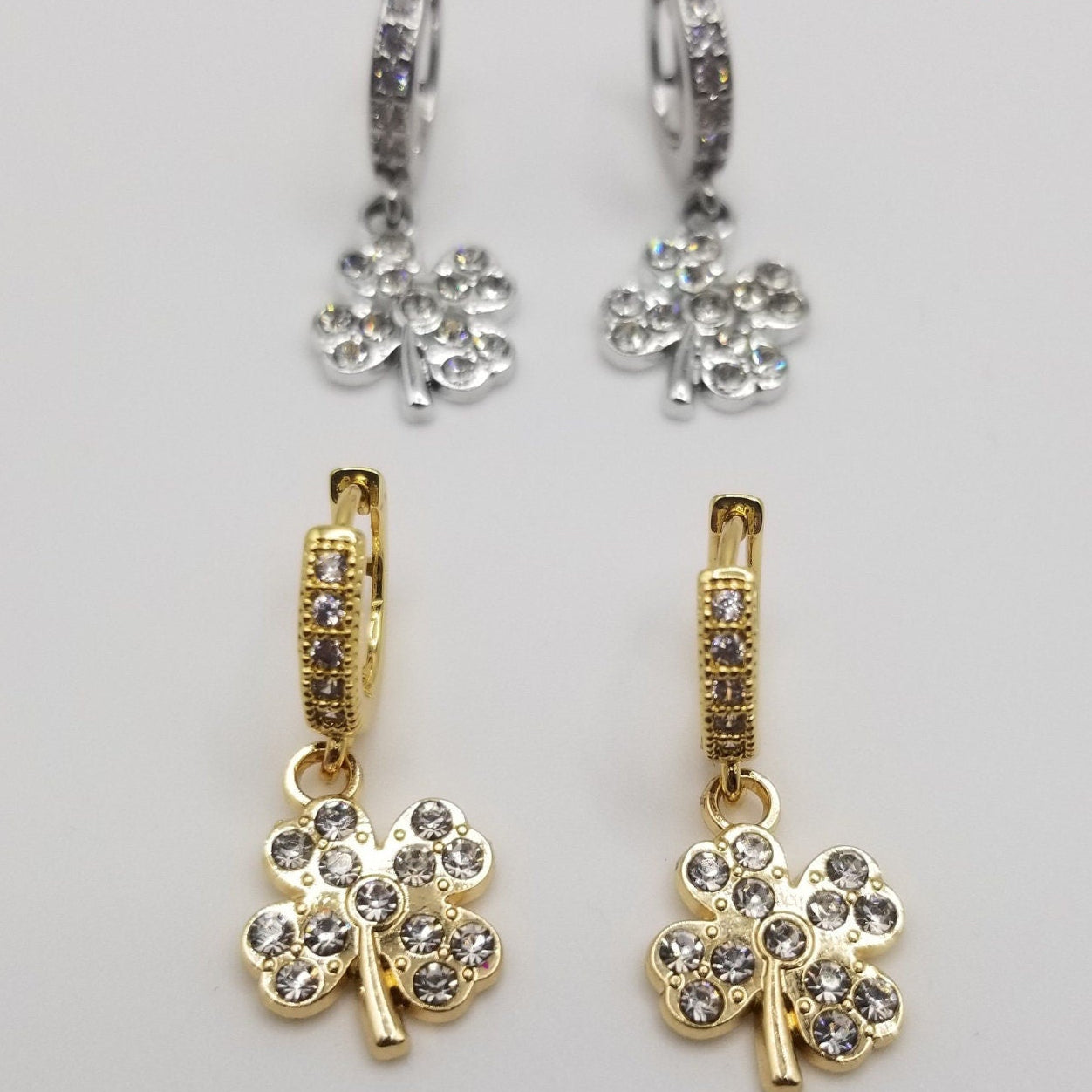 Gold and silver clover shaped earrings with cubic zirconia detailing on charms and Huggie closures.