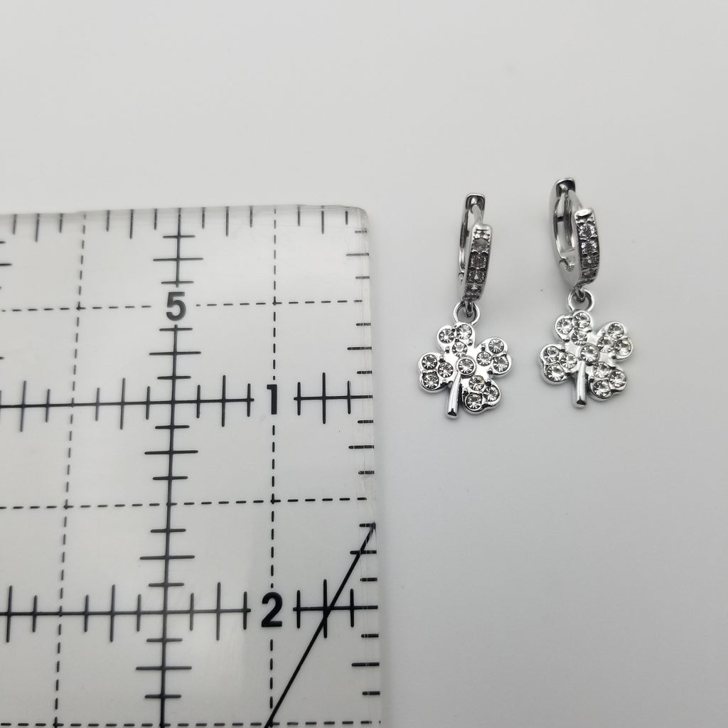 Silver shamrock earrings on a gray surface with a ruler for scale.
