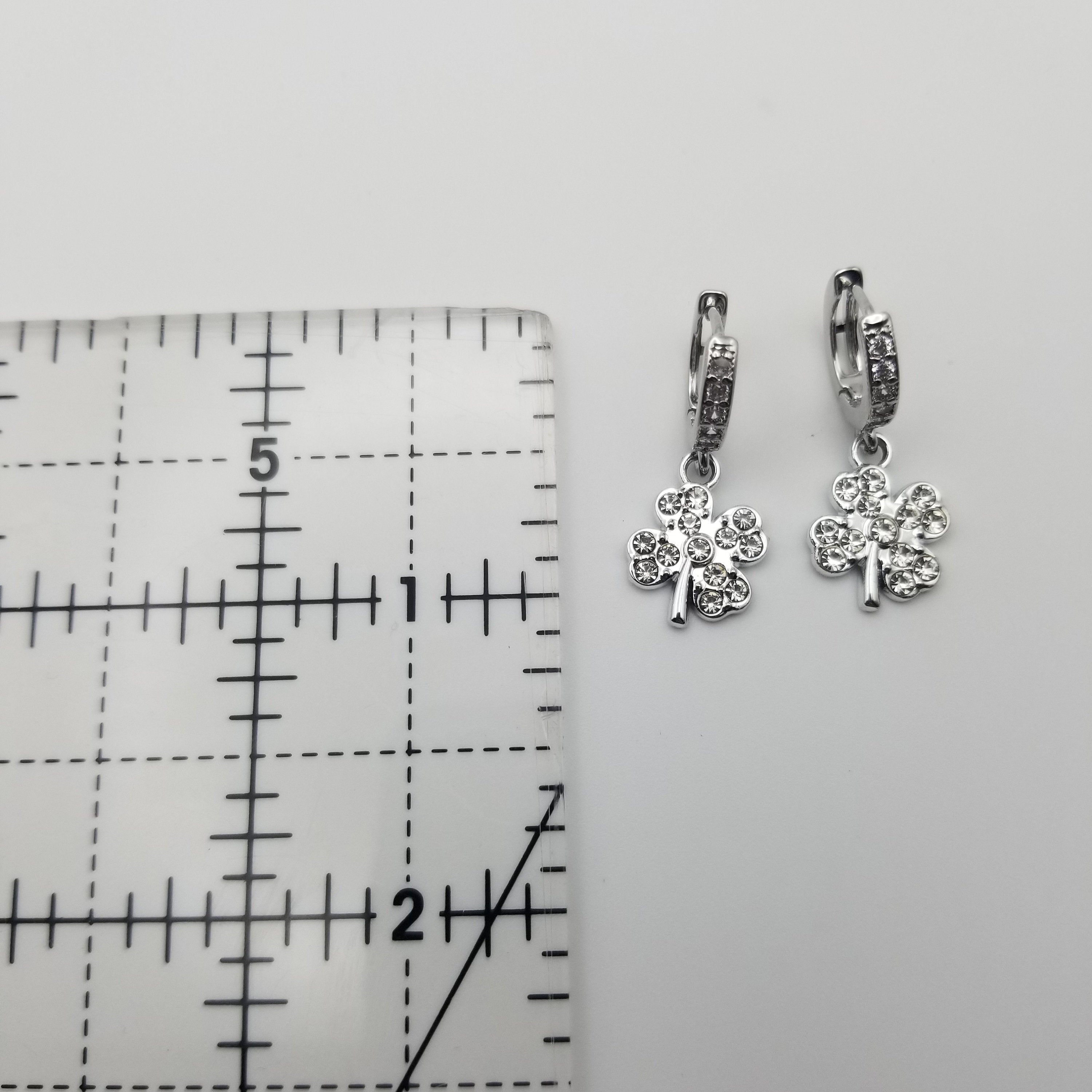 Silver shamrock earrings on a gray surface with a ruler for scale.