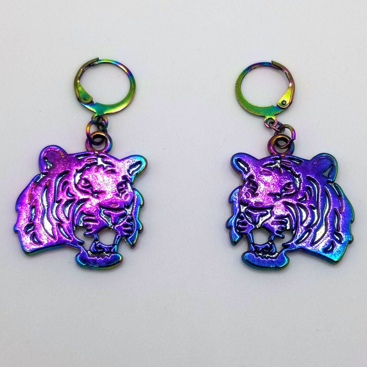 Rainbow iridescent tiger shaped Huggie earrings on a light gray background