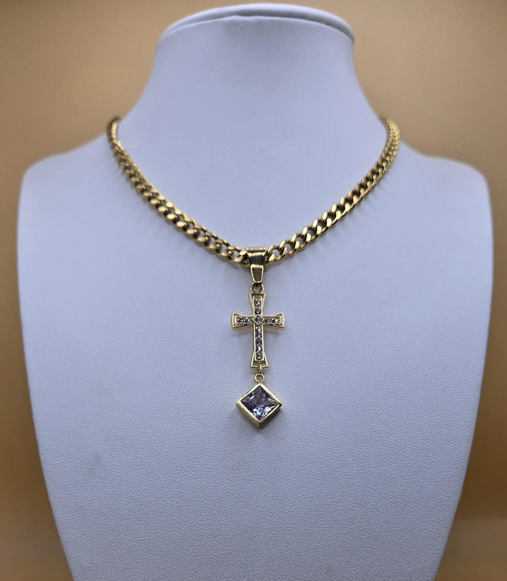 A statement 18k gold-plated ornate cross necklace displayed on a white jewelry mannequin. The design features a cross set with shimmering cubic zirconia and a large square-cut crystal drop pendant on a bold Cuban link chain.